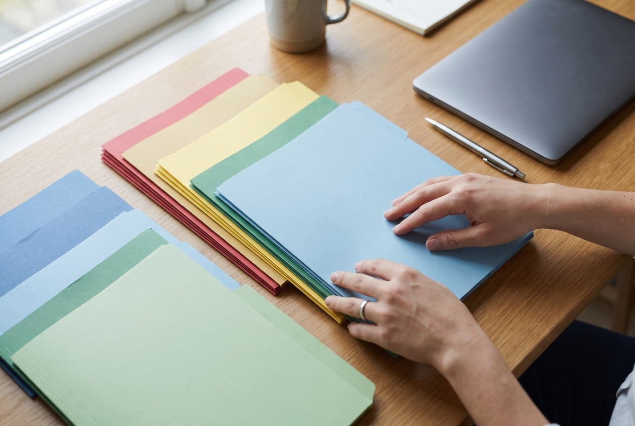 Mains classant des chemises de couleurs en rangées ordonnées sur un bureau, l'hygiène de rangement qui rend un conteneur lisible par quelqu'un qui le découvre