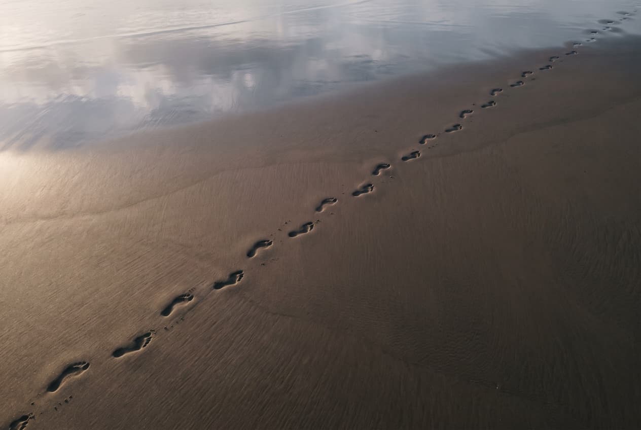 Traces de pas sur le sable humide vues du dessus, image du parcours post-clic que révèle le fait de relier Google Ads et GA4