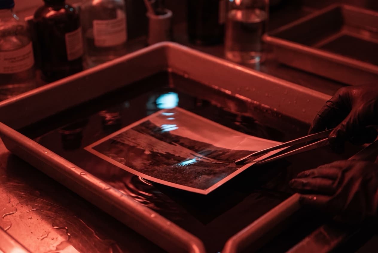 Tirage photo qui apparaît lentement dans un bain révélateur sous la lumière rouge d'un laboratoire, image du temps d'apprentissage avant de juger le ROI d'une campagne SEA